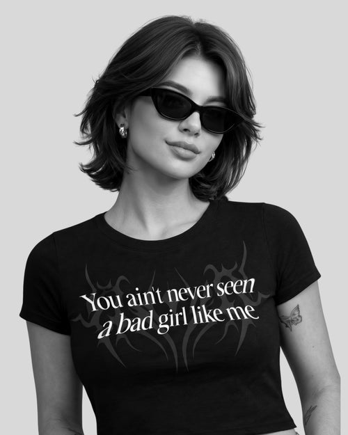 Woman wearing black aesthetic crop top with bold bad girl quote graphic, gen z streetwear fashion inspired by underground rap reble vibe and dhurandhar cinematic aesthetic, Edgy gen z outfit with black bad girl crop top, confident aesthetic streetwear look inspired by underground rap culture and dhurandhar style fashion